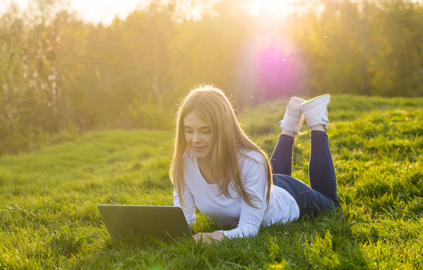 Νεαρή όμορφη γυναίκα φοιτητής με ένα φορητό υπολογιστή βρίσκεται στο γρασίδι, εγώ - Φωτογραφία, εικόνα