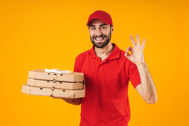 Portrait of positive delivery man in red uniform showing ok sign - Foto, Imagen