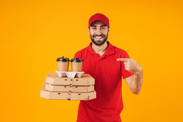 Portrait of attractive delivery man in red uniform holding pizza - Fotoğraf, Görsel