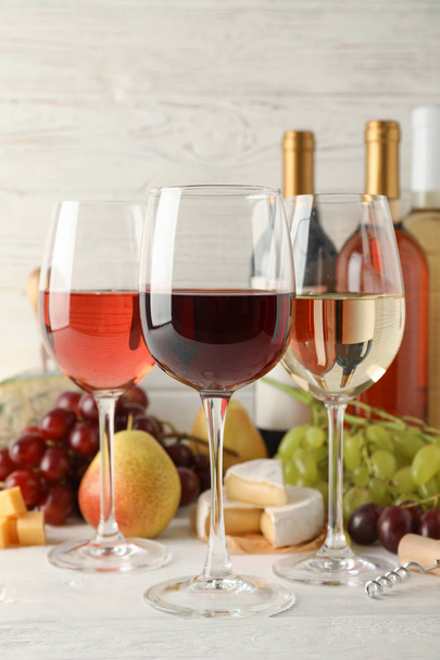 Fruit, kaas, flessen en glazen met verschillende wijn op wit - Foto, afbeelding