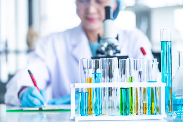 asiatische Wissenschaftlerin bei der Vorbereitung von Laborgeräten wie Gläsern, Röhren mit blauer Flüssigkeit auf dem weißen Tisch. das chemische Experiment in der wissenschaftlichen Forschung - Foto, Bild