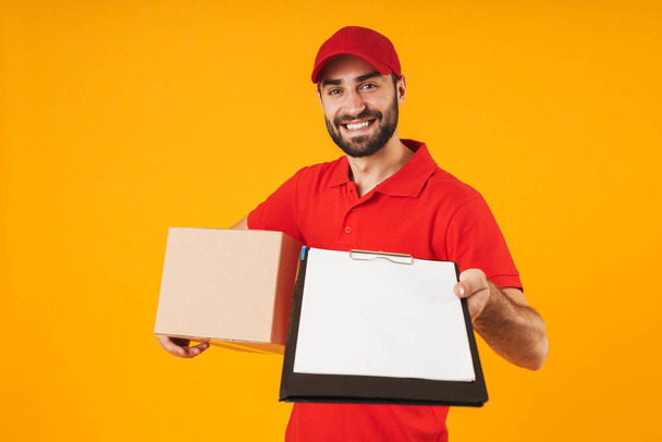 Image of caucasian delivery man in red uniform holding clipboard - Foto, afbeelding