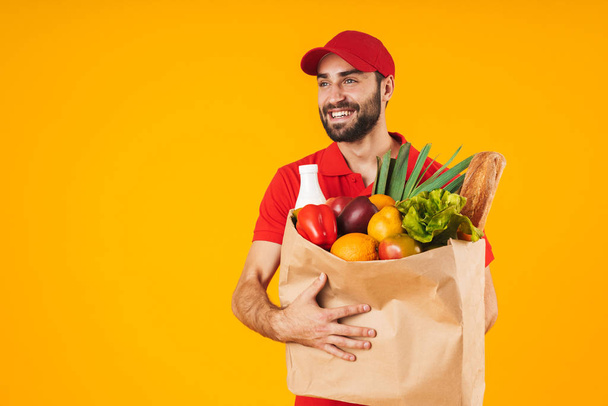 Portrait of attractive delivery man in red uniform smiling while - Foto, imagen