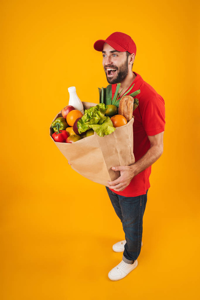 Portrait of unshaven delivery man in red uniform smiling while c - Photo, Image