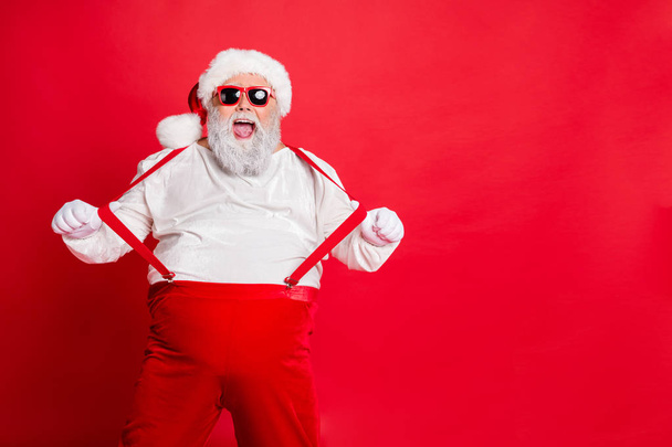 Portrait of funny fat overweight santa claus with big belly abdomen forever young touch his suspenders scream fool wearing trousers pants isolated over red background - Photo, Image