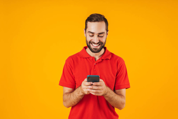 Portrait of joyful man in red t-shirt smiling and holding smartp - Φωτογραφία, εικόνα