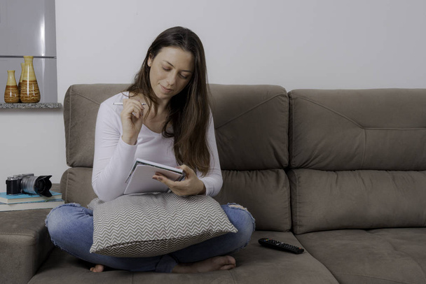 Beautiful woman sitting on the couch making notes in a notebook. - Photo, Image