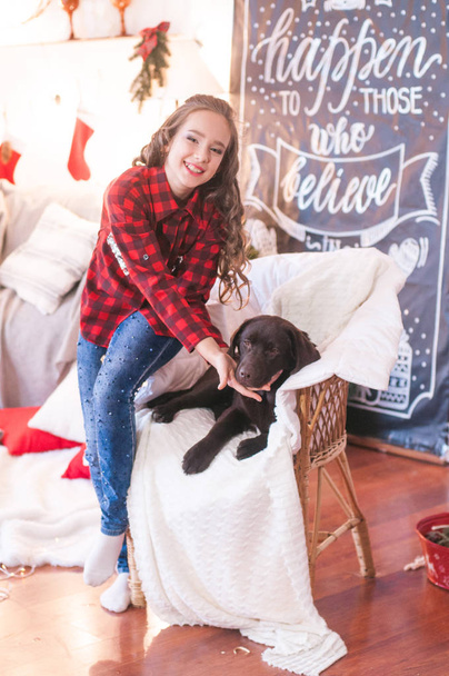 Cute girl in a red checkered shirt  with dog labrador at home in the room decorated for Christmas. Happy christmas mood - Fotografie, Obrázek