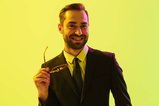 Cheery smiling happy young business man posing isolated over light green background wall with led neon lights. - Фото, изображение