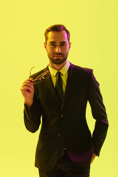 Optimistic young business man posing isolated over light green background wall with led neon lights holding glasses. - Фото, зображення