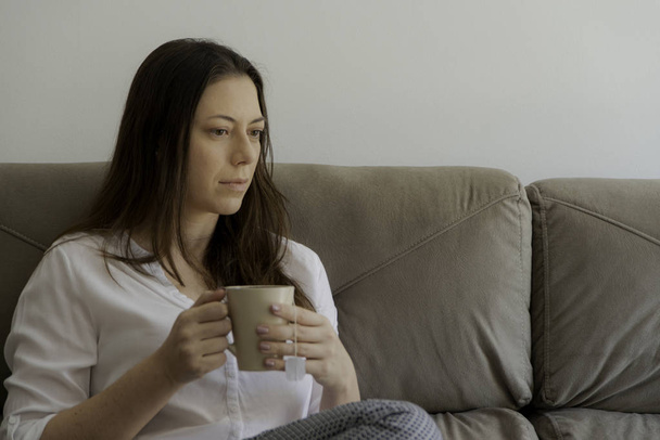 Tired woman sitting on the couch having tea. - Фото, зображення