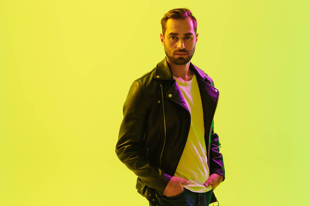 Handsome young stylish man posing isolated over light green background wall with led neon lights dressed in leather jacket. - Valokuva, kuva
