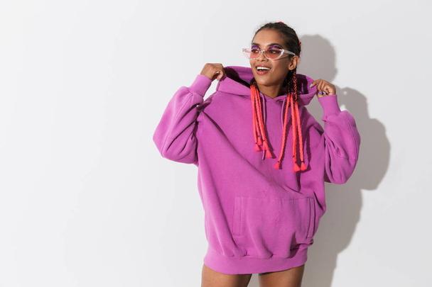 Smiling cheery happy young african stylish woman in pink sweatshirt and sunglasses posing isolated over white wall background. - Valokuva, kuva