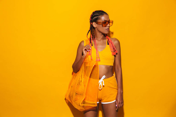 Image of attractive african american woman wearing sunglasses standing and carrying plastic bag - 写真・画像