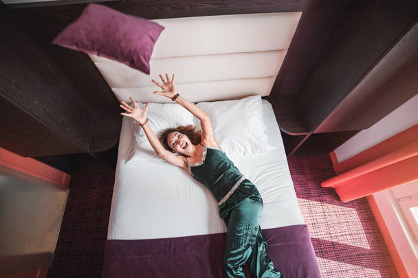 大きなベッドに横たわって枕を投げる美しい若い女性 - 写真・画像