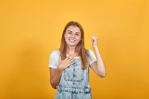Молодая женщина в белой футболке, на оранжевом фоне показывает эмоции
 - Фото, изображение