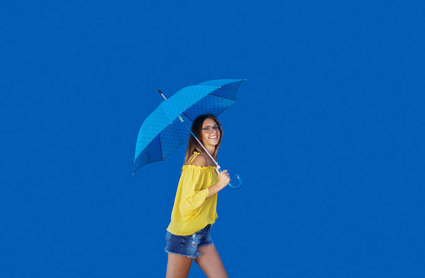 青い傘で歩く黄色いブラウスで美しい笑顔白人十代の少女. - 写真・画像