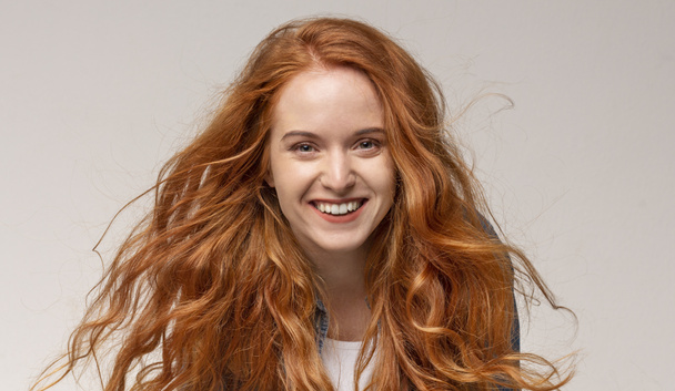 Beautiful redhead girl laughing, looking at camera on light background - 写真・画像