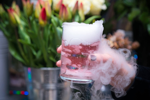 Beautiful woman holding dry ice cocktail at the party. Purple cocktail drink with ice vapor at the club - Photo, Image
