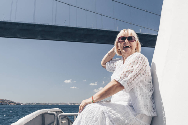 Lächelnde attraktive Frau mit Sonnenbrille auf dem großen weißen Schiff oder der Jacht. Kreuzfahrt, Reisen und Abenteuer für aktive Rentner. schönes blaues Meer auf dem Hintergrund. - Foto, Bild