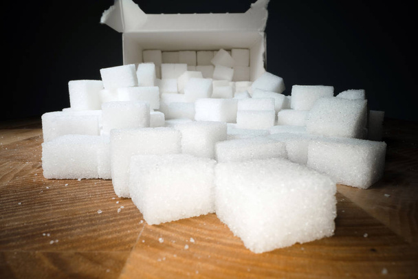 Macro shot di cubetti di zucchero accanto alla scatola di cartone sul tavolo di legno. Dolcificante alimentare malsano, cubi di cristallo dolce
 - Foto, immagini