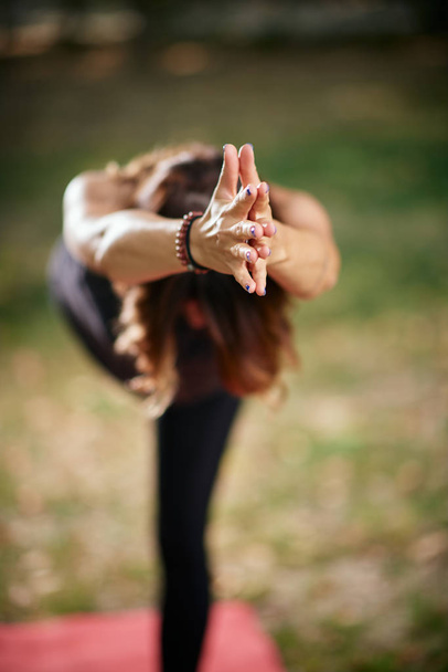 fokussierte kaukasische Frau in Krieger-Iii-Yoga-Pose. Natur außen. Selektiver Fokus auf die Hände. - Foto, Bild