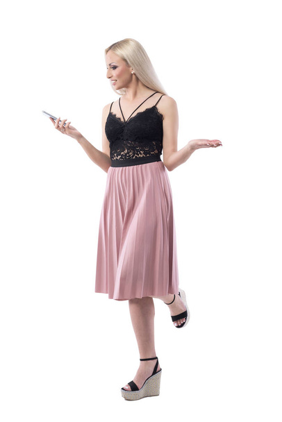 Confused young blonde woman using smart phone shrugging with arms up. Full body isolated on white background. - Photo, Image