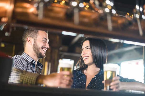 Young couple at beginnings of love story - Pretty woman drinking beer with handsome man at pub - Relationship lovers concept with drunk boyfriend and girlfriend together at brewery - Warm retro filter - Foto, Bild