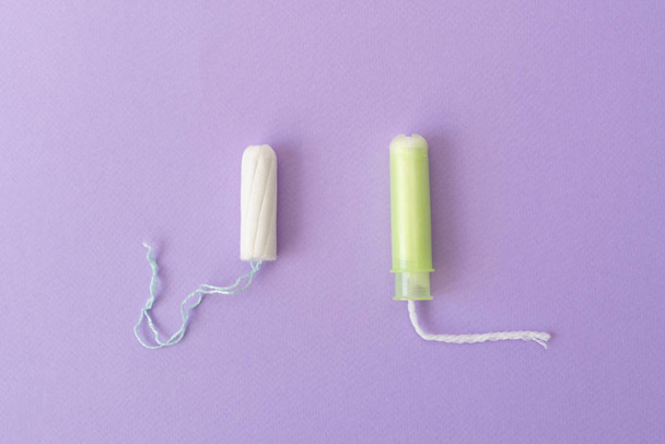 Twee katoenen tampons met licht groene applicator en zonder applicator op een violet achtergrond. Hygiënische soorten tampons. Menstruatie, bescherming, vergelijkings concept, platte lay, kopieer ruimte, bovenaanzicht - Foto, afbeelding