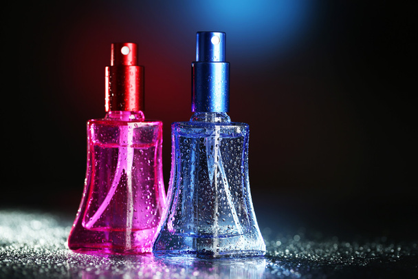 Women perfume in beautiful bottles on dark background with color light - Фото, изображение
