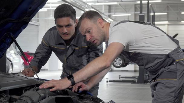 Auto mechanics discuss broken car at their garage looking under the hood - Foto, Bild