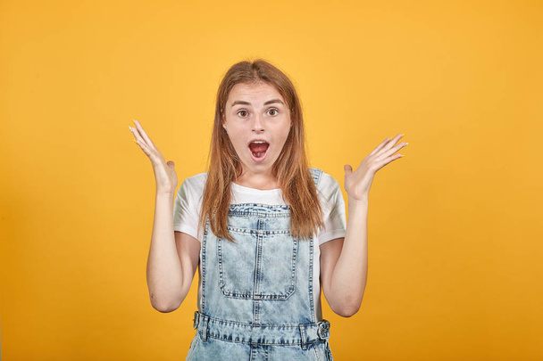 Jonge vrouw draagt wit t-shirt, over oranje achtergrond toont emoties - Foto, afbeelding