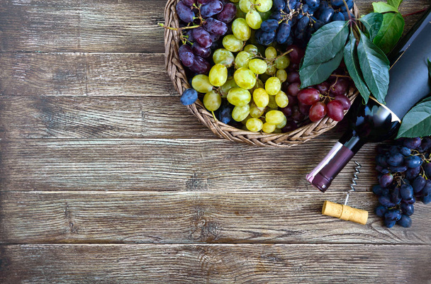 Botella con vino tinto, sacacorchos, uvas azules en cesta, hojas en una mesa de madera. Fondo de vino con espacio de copia. Vista superior, plano
 - Foto, imagen