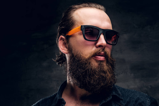 Bearded man in sunglasses is posing for photographer at dark photo studio. - Photo, Image