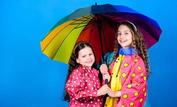 Walk under umbrella. Kids girls happy friends under umbrella. Rainy weather with proper garments. Happy childhood. Bright umbrella. It is easier to be happy together. Be rainbow in someones cloud - Photo, image