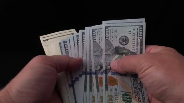 Mies laskee dollareita mustalla pohjalla. Miehen käsissä on nippu amerikkalaista rahaa. Tarkistan satasen seteleitä väärennöksen varalta. Käsite: rikkaus, rikastuminen, väärennetyn rahan todentaminen
. - Materiaali, video