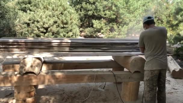 Pracownik poleruje Deski sosnowe z narzędziem szlifierki. W rękach człowieka jest narzędziem do szlifowania i polerowania powierzchni drewnianej deski. Rzemieślnik z drewna pracuje własnymi rękami. - Materiał filmowy, wideo