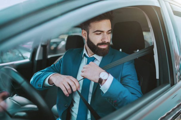 彼の高価な車に座っている間、若い魅力的な責任あるビジネスマンはシートベルトを締める. - 写真・画像