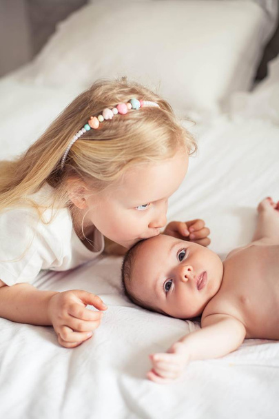 Young beautiful mother holds a baby. Little sister kisses her little sister. Baby. Children bedroom. - Foto, imagen