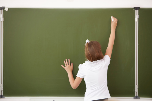 Scoolgirl standing near blackboard - 写真・画像