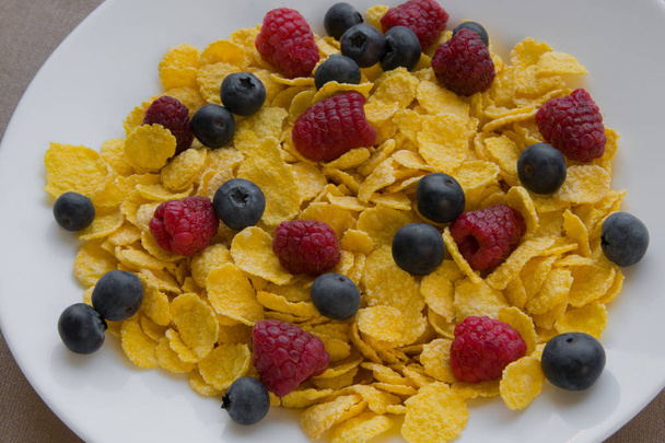 Corn flakes with fresh raspberries and blueberries in a white plate - 写真・画像