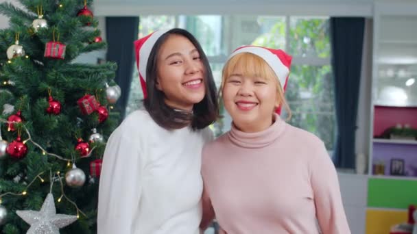 Asiatique Lesbienne couple célébrer Noël festival. LGBTQ adolescent féminin porter chapeau de Noël se détendre heureux sourire en regardant la caméra profiter de Noël vacances d'hiver ensemble dans le salon à la maison
. - Séquence, vidéo