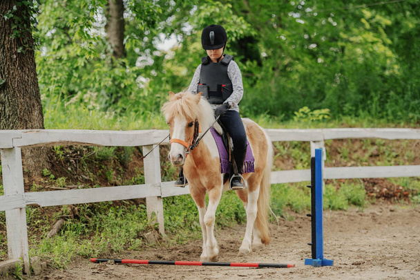 Giovane ragazza caucasica giocosa con casco e giubbotto protettivo a cavallo cavallo adorabile pony al ranch. pony saltare ostacolo. - Foto, immagini
