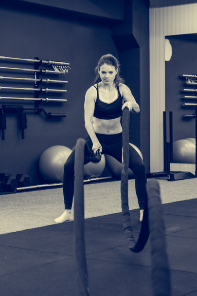 Молода атлетична жінка займається в тренажерному залі з використанням бойової мотузки
. - Фото, зображення