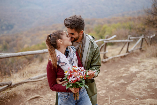 Veselý, roztomilý multikulturní pár, oblečený v přírodě a v objetí. Žena držící květiny. Podzimní sezóna. - Fotografie, Obrázek