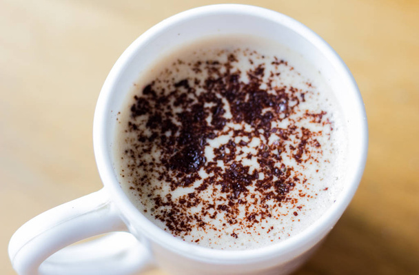 Cappuccino valkoisessa mukissa. Kahvia vaahdolla ja suklaamukilla valkoisessa mukissa. Hyvää huomenta. Huomenta cappuccino aamiaiseksi. Kahvi muki alkuun näkymä
. - Valokuva, kuva