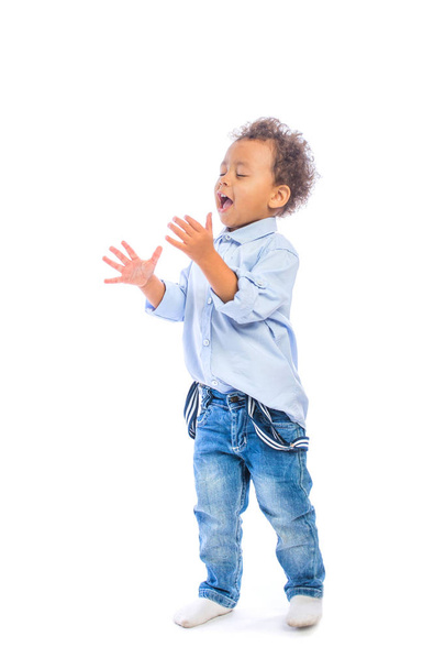 A small dark-skinned baby with curly hair is cheering, something screams having closed his eyes and stretching his arms upwards, bent at the elbows, an isolated background - Foto, imagen
