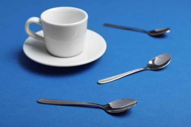 Teaspoons and cup with saucer on blue background - Zdjęcie, obraz