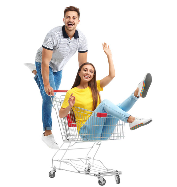 Young couple with shopping cart on white background - Фото, изображение