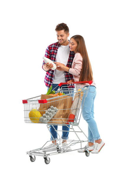 Young couple with full shopping cart on white background - Foto, imagen